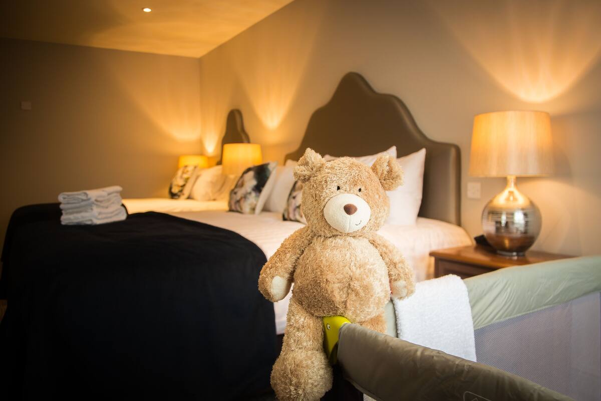 A hotel room with a bed, a bedside lamp, a teddy bear, and a nightstand.