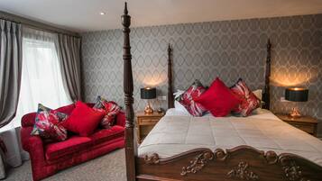 A four-poster bed with red and white bedding, a red sofa with floral cushions, and two bedside tables with lamps.