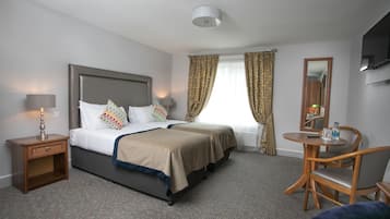 Habitación de hotel con cama doble, mesitas de noche, un escritorio con silla, un espejo y una ventana con cortinas.