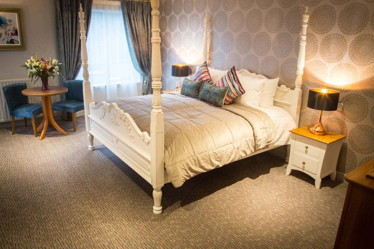 A four-poster bed with a canopy, a bedside table with a lamp, and a small round table with a vase of flowers.