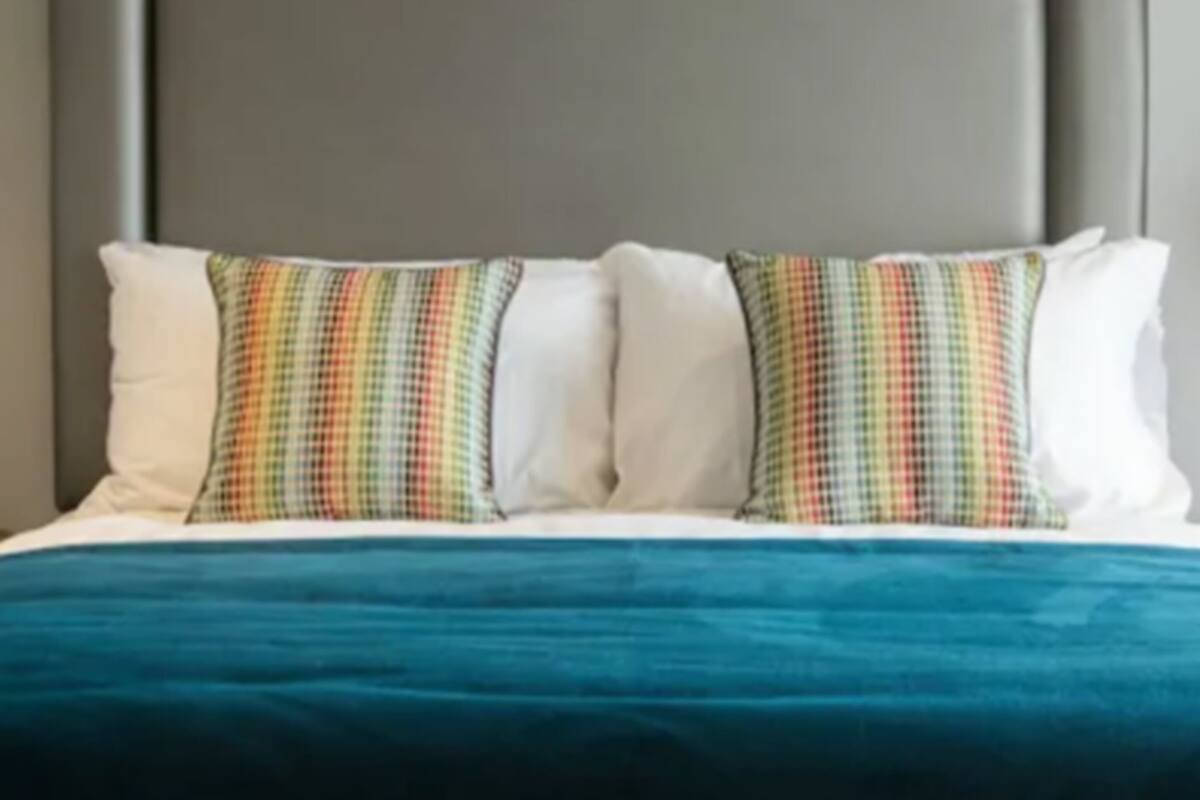 A bed with a grey headboard, white pillows, and a teal bedspread.
