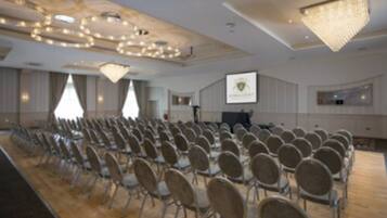 Un salón de conferencias con filas de sillas, una pantalla de proyector y una araña.