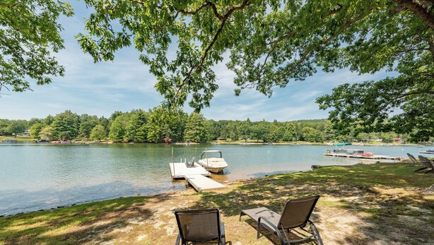 A lakeside view with two chairs facing the water, docked boats, and a grassy area. - Cape Cod Charm w/ Dock Slip & Fire Pit (Swanton)