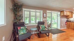 A room with two grey armchairs, a small round table, a large window, and a view of the outdoors. - Cape Cod Charm w/ Dock Slip & Fire Pit (Swanton)