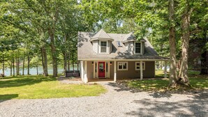 A house with a red door, a covered porch, and a gravel driveway. - Cape Cod Charm w/ Dock Slip & Fire Pit (Swanton)