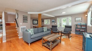 A spacious living room with hardwood flooring, a gray sofa, a wooden coffee table, and a bookshelf. - Cape Cod Charm w/ Dock Slip & Fire Pit (Swanton)