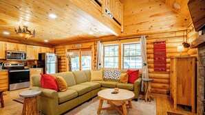 Ein Holzblockhaus-Interieur mit einer Küche, einem Ecksofa, einem runden Couchtisch und einem Essbereich.