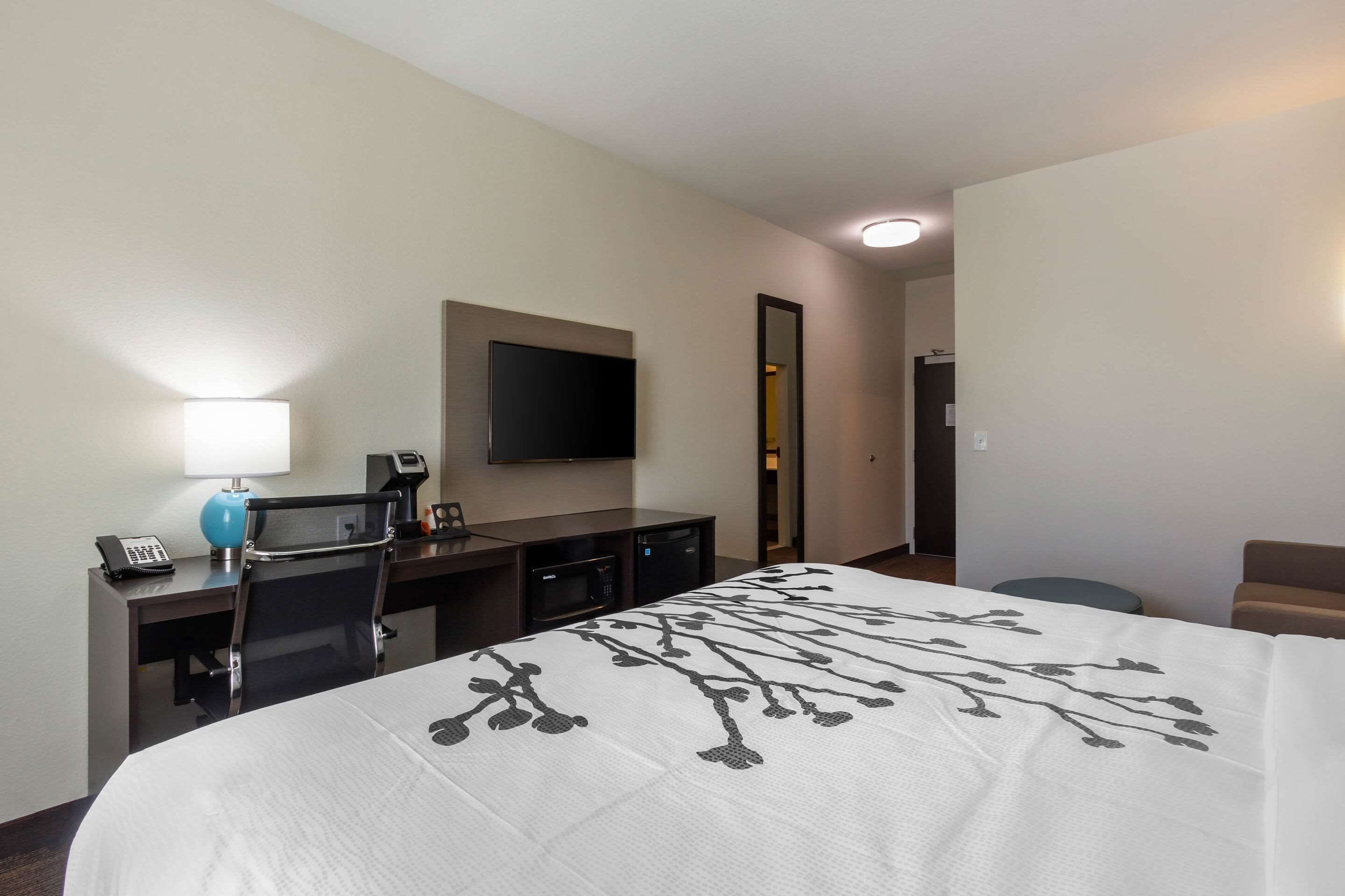 Habitación de hotel con cama, escritorio con lámpara, microondas, teléfono y televisor en la pared.