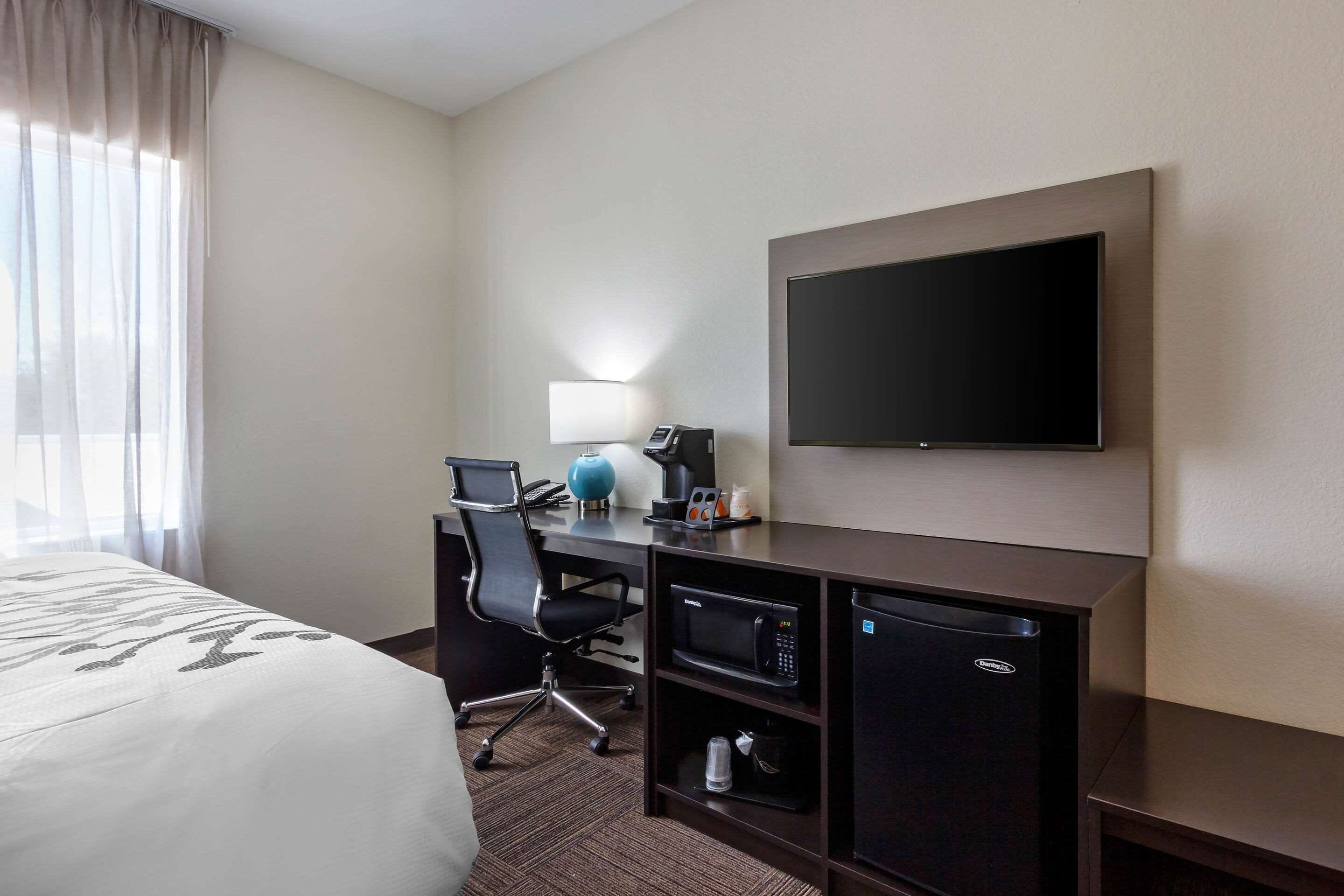 A hotel room with a bed, a desk with a computer, a microwave, a coffee maker, and a TV.