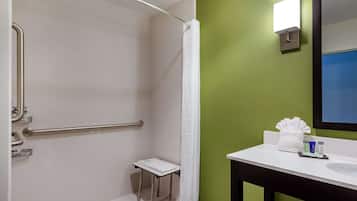 A bathroom with a shower, grab bar, small step stool, and a sink with toiletries.