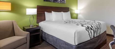 A hotel room with a bed, a sofa, a nightstand, and a lamp.