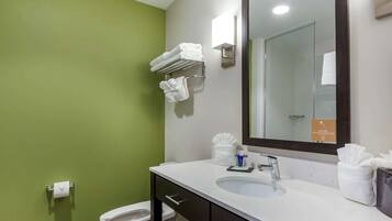 A bathroom with a green wall, white sink, and a mirror. There are towels on a rack and a toilet.