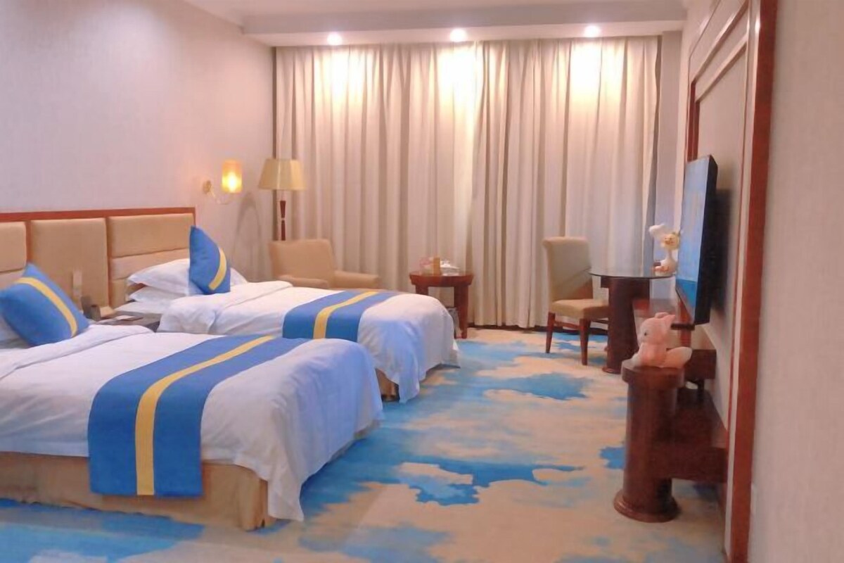 Una habitación de hotel con dos camas, televisión, escritorio y una silla.
