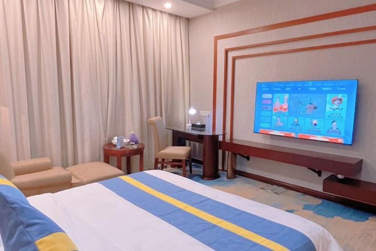 A hotel room with a bed, a desk, a chair, a television, and curtains.
