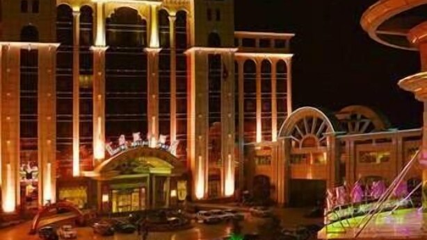 A large hotel with multiple floors, a prominent entrance, and a parking lot with several cars. - King We Holiday Hotel (Quanzhou)