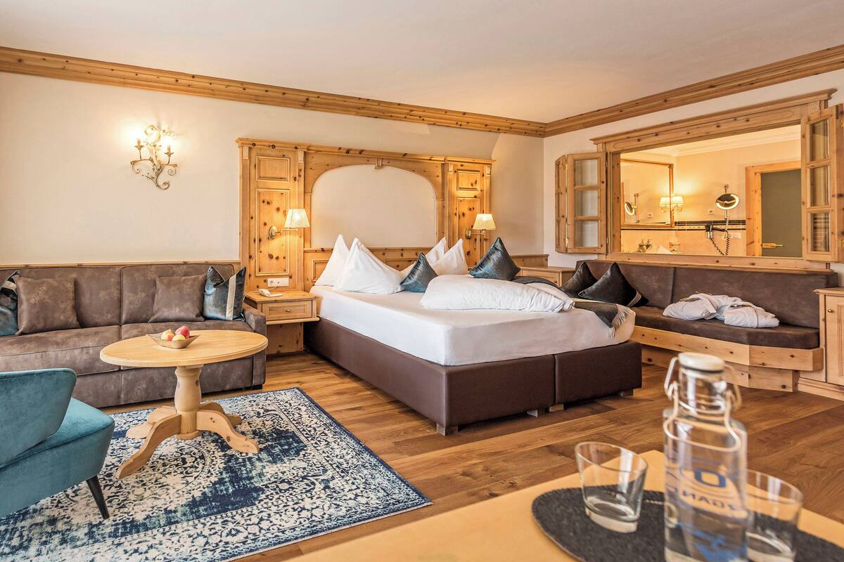 Une chambre d’hôtel comprenant un lit, un canapé, une petite table, une chaise, un miroir et une armoire en bois.