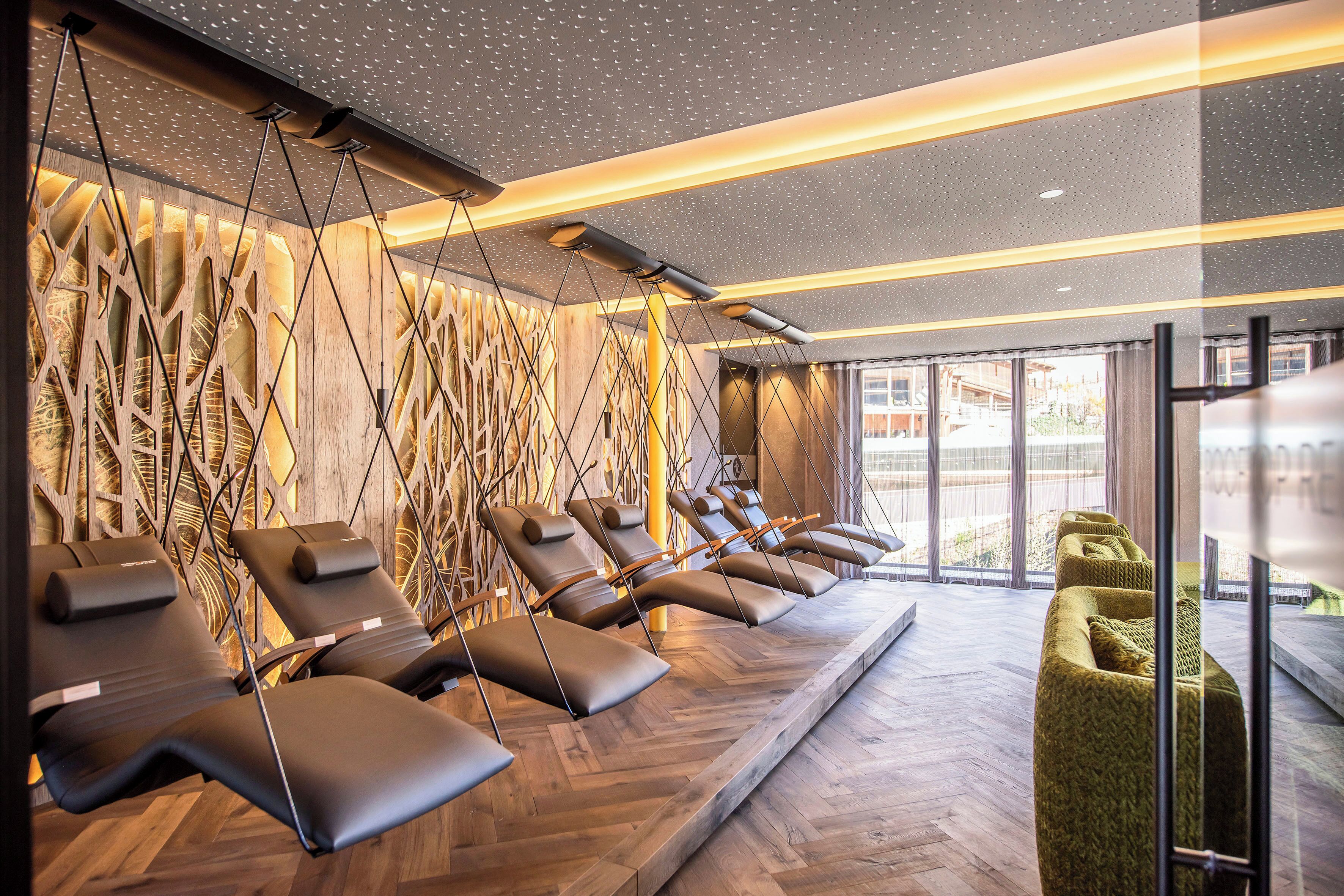Un espace spa moderne doté de plusieurs fauteuils de massage, d’un mur en bois au design original et d’une grande fenêtre laissant entrer la lumière naturelle.