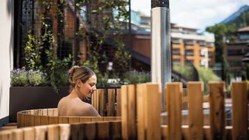 A spa area with wooden benches, a metal column, and a view of buildings and greenery.