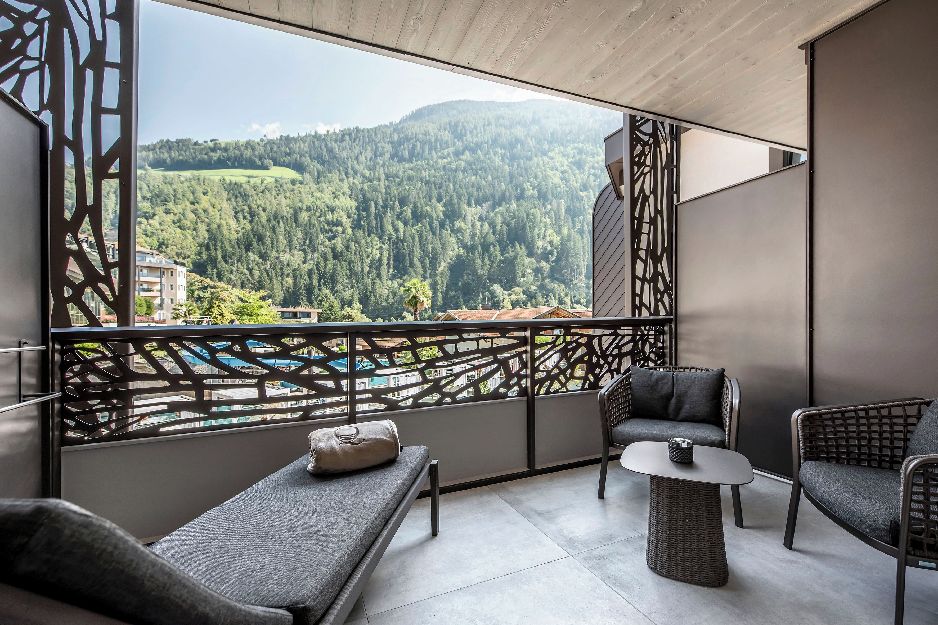 Ein Balkon mit Blick auf einen bewaldeten Berg, Korbmöbel und ein Schwimmbad.