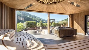 Un interior moderno con un banco de madera curvado, una chimenea y un gran ventanal que da a un patio exterior con asientos y vistas a un paisaje montañoso.
