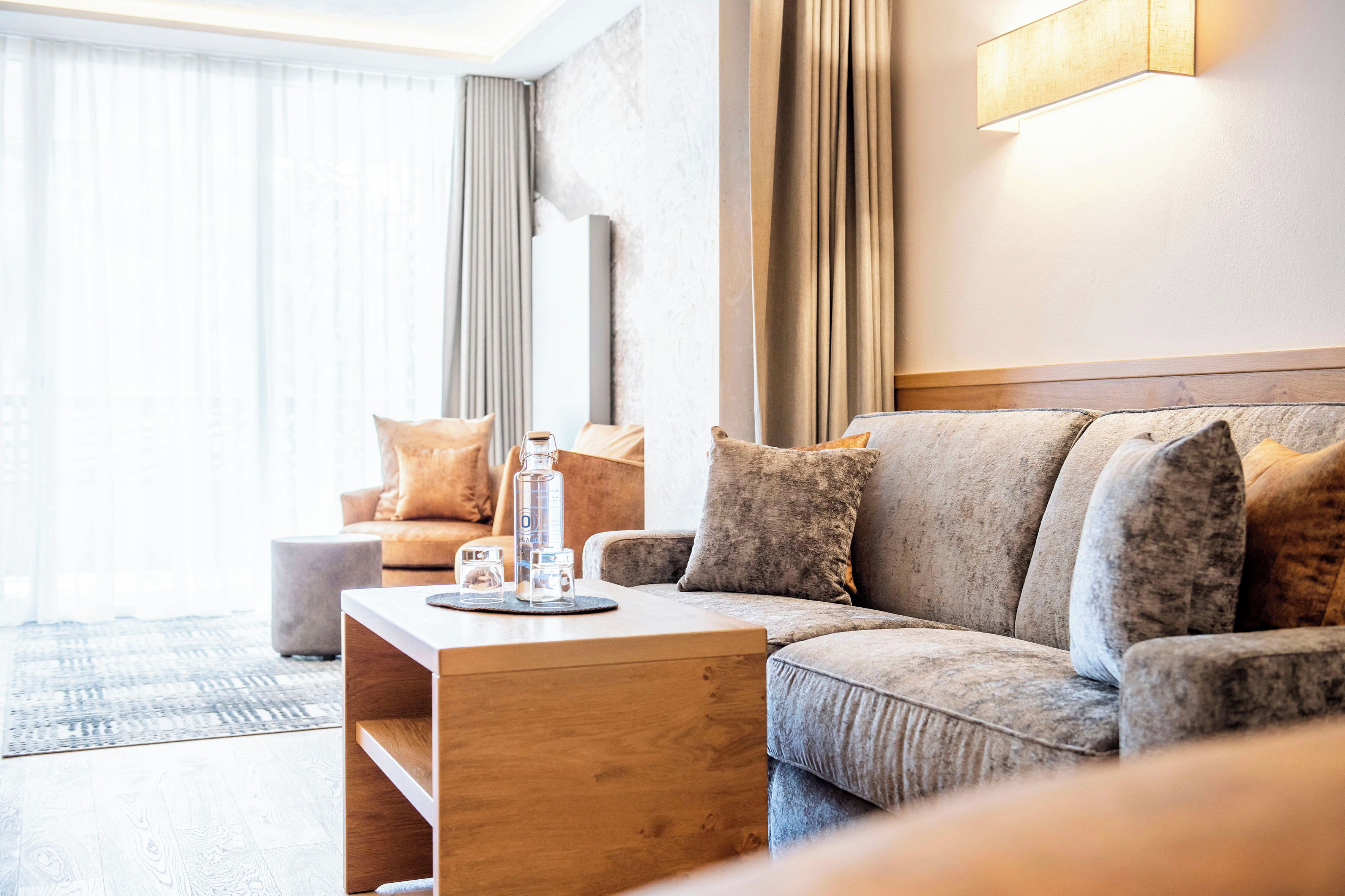 A modern living room with a grey sofa, a wooden coffee table, and a grey ottoman.
