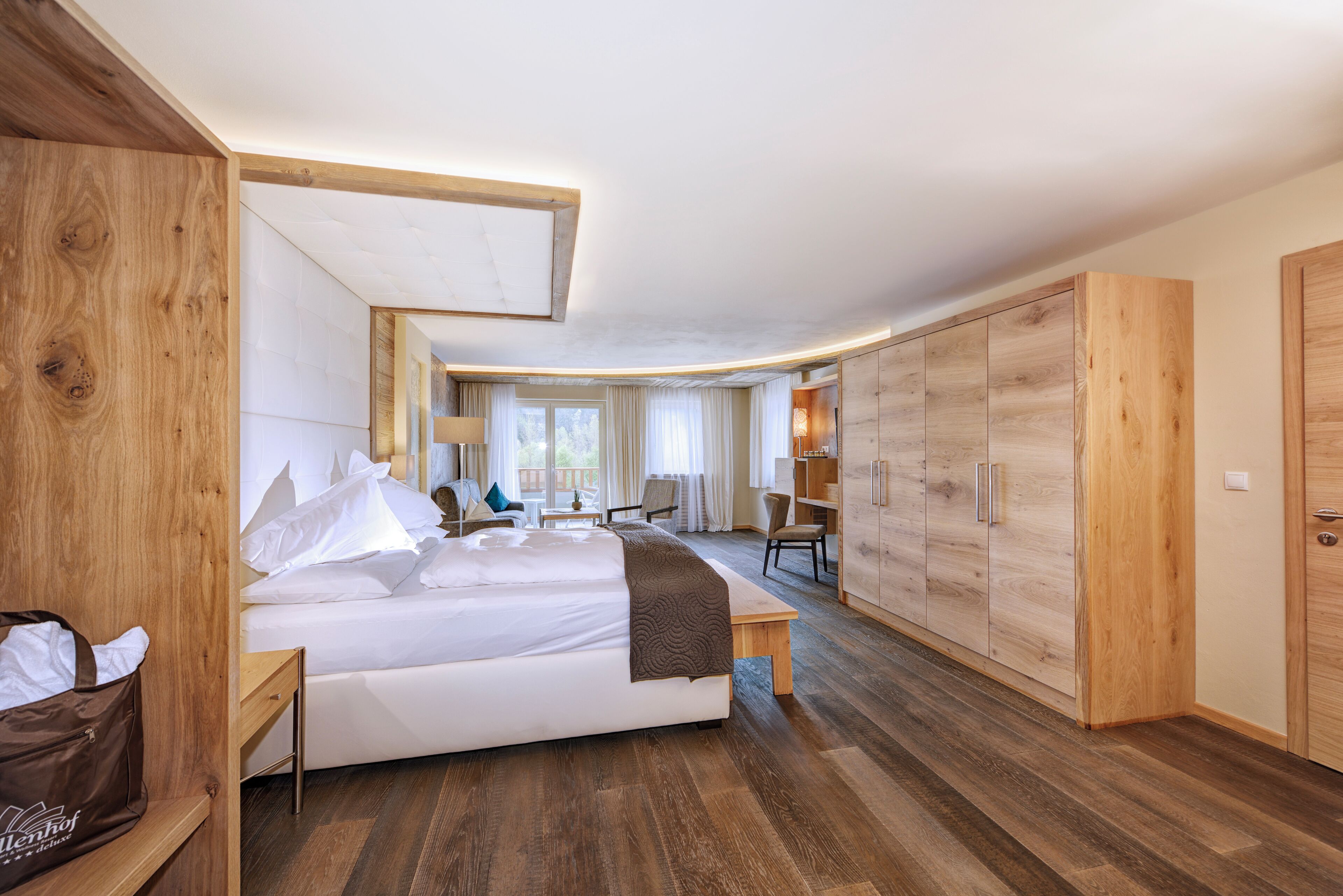 A modern hotel room with a large bed, wooden wardrobe, and a desk area.