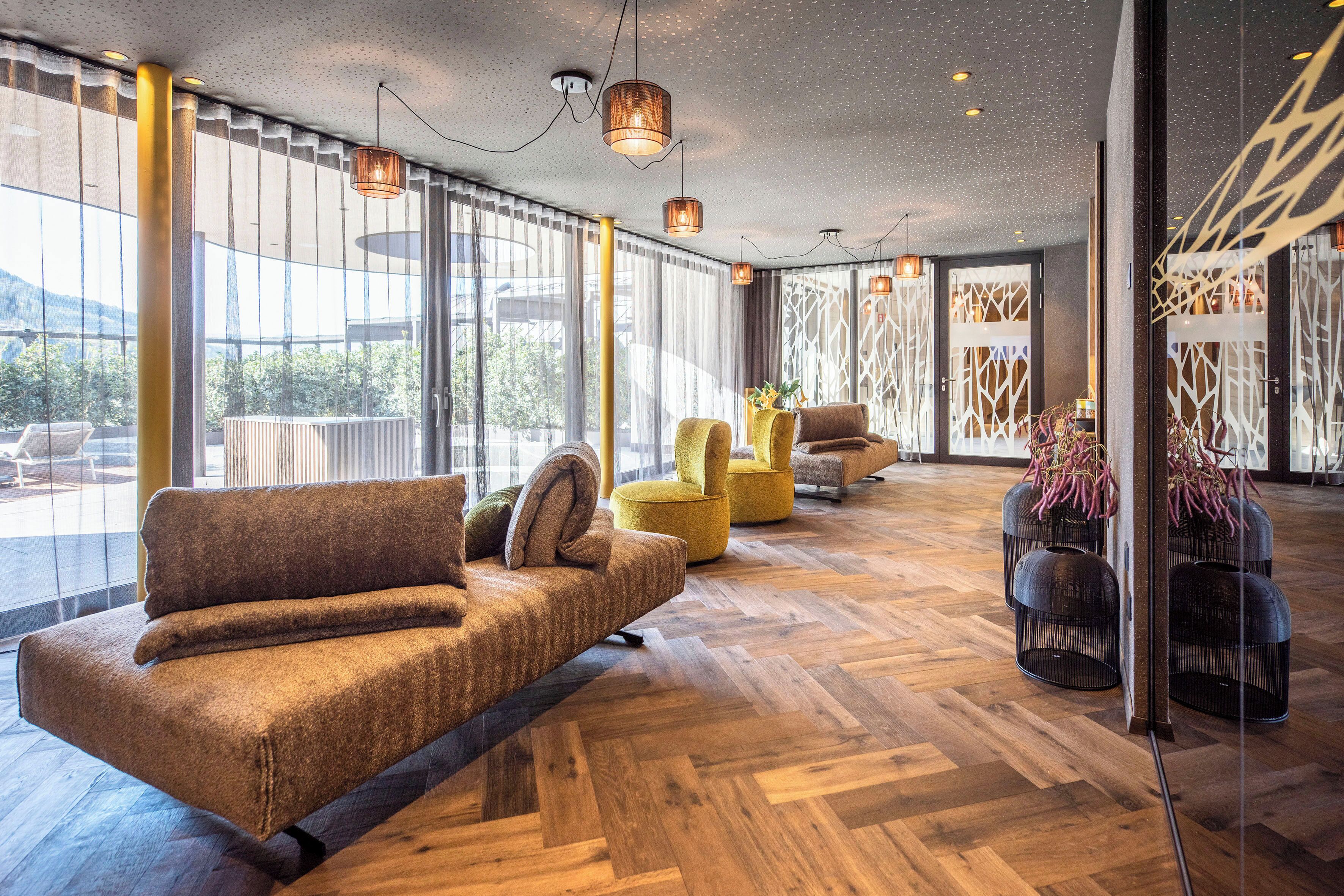 A modern interior with a wooden herringbone floor, a brown sofa, yellow chairs, and hanging pendant lights.
