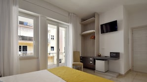 Habitación de hotel con cama, escritorio, silla, televisor y balcón con vista a la ciudad.