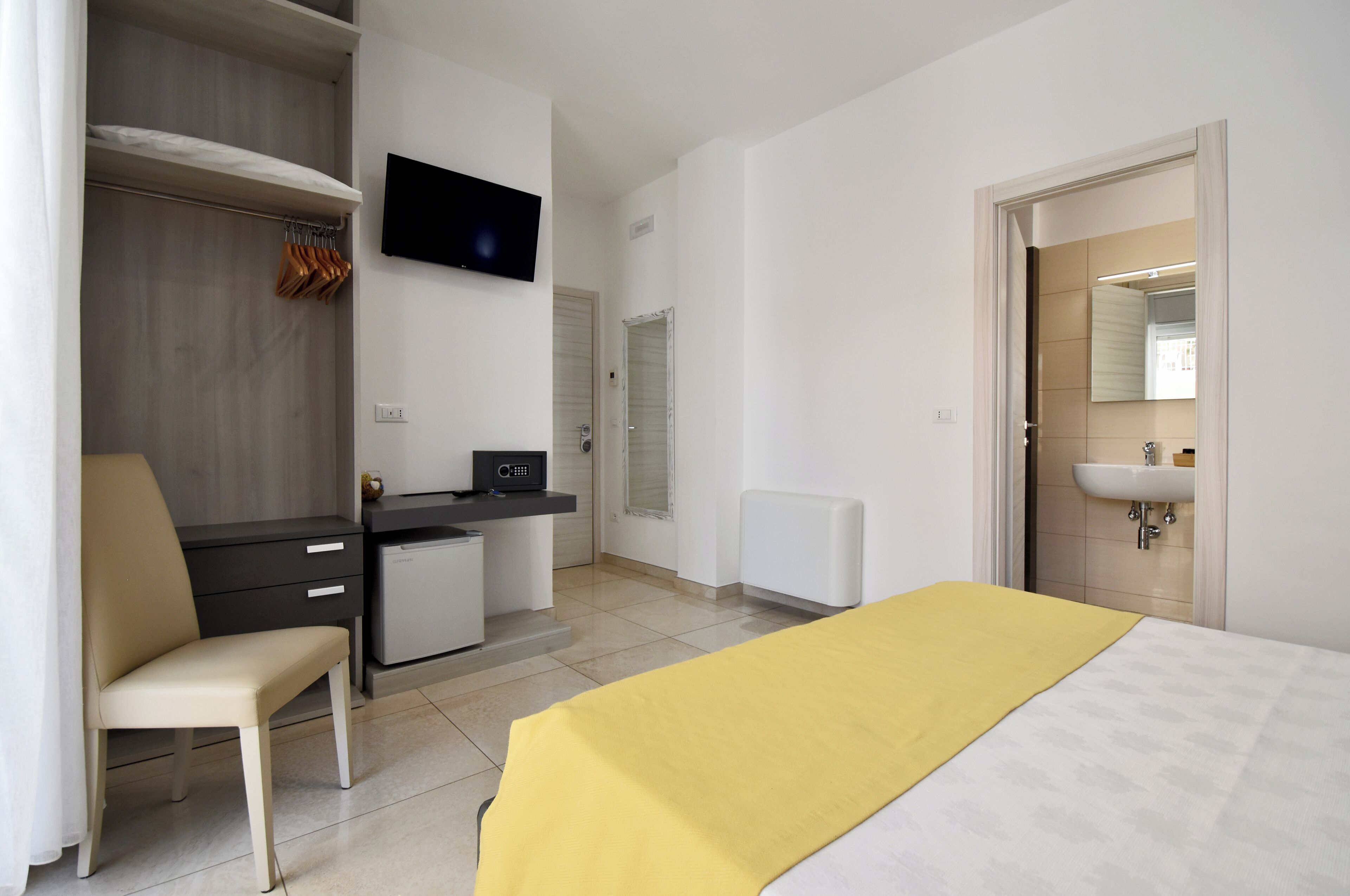 A hotel room with a bed, a desk, a chair, a TV, a wardrobe, and a bathroom with a sink.