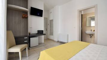 A hotel room with a bed, a desk, a chair, a TV, a wardrobe, and a bathroom with a sink.