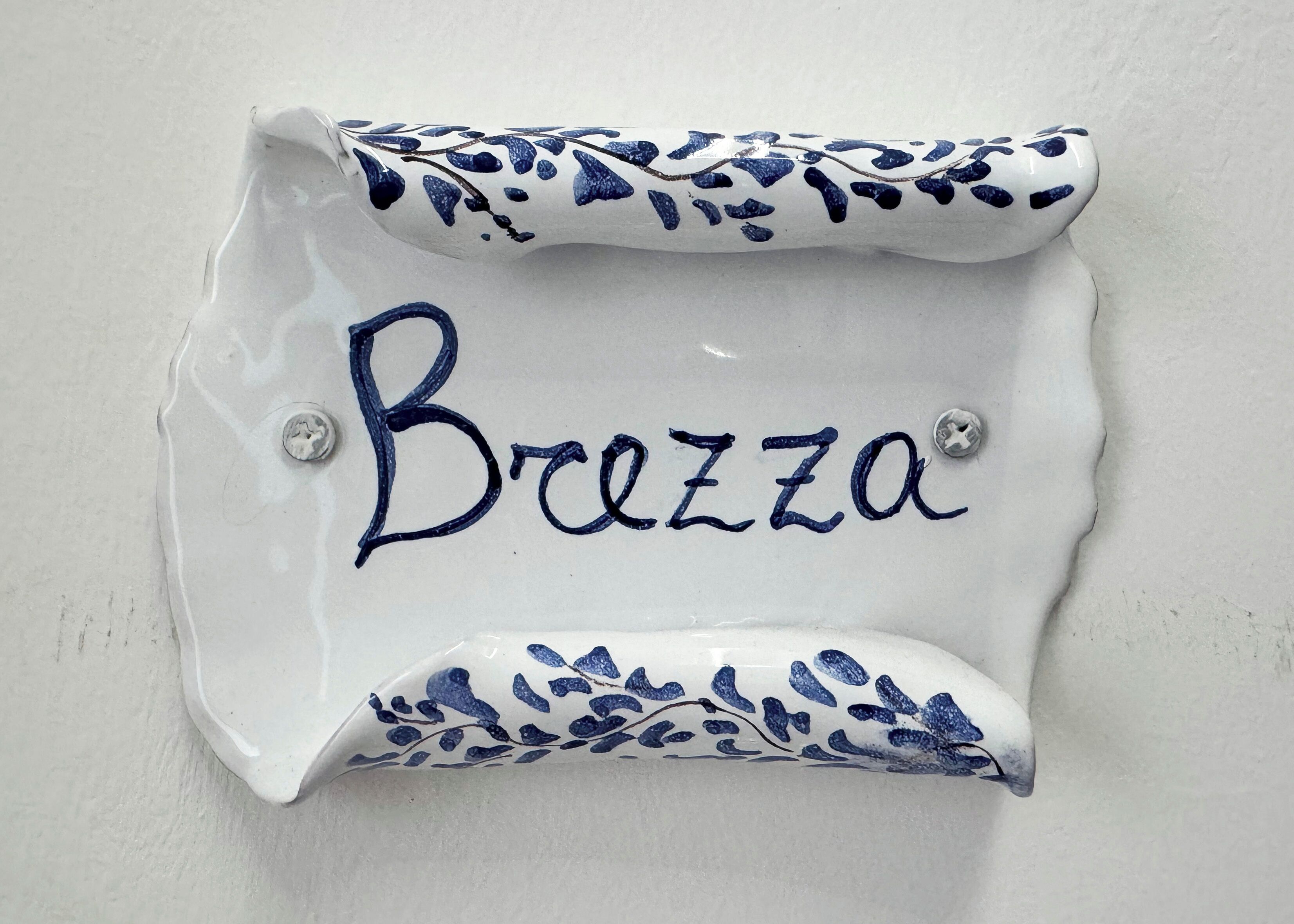 A ceramic wall decoration with the word "Breeza" written in cursive.
