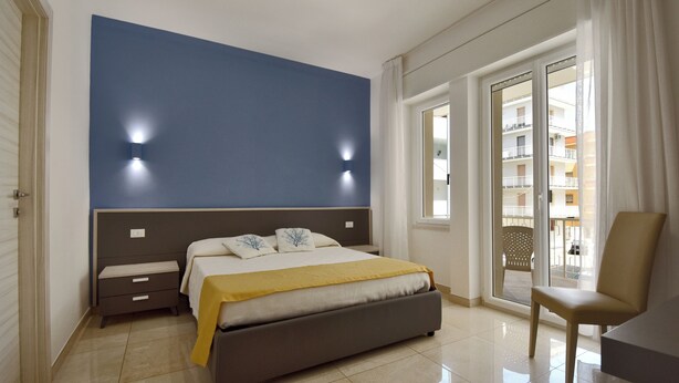 Un dormitorio con cama, mesitas de noche, una silla y vistas a un balcón exterior.