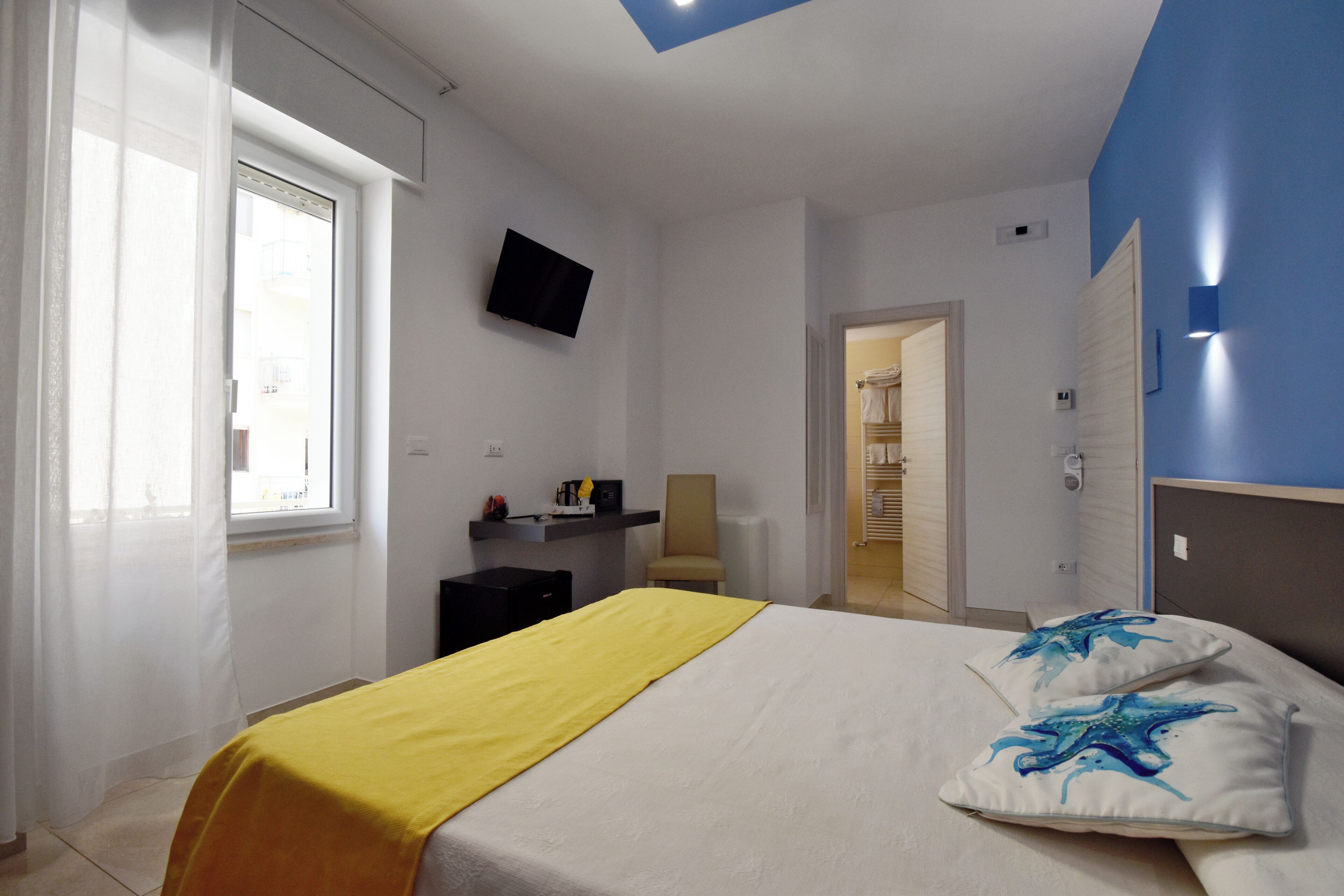 Een slaapkamer met een bed, een televisie aan de muur, een raam met gordijnen en een deur naar een badkamer.