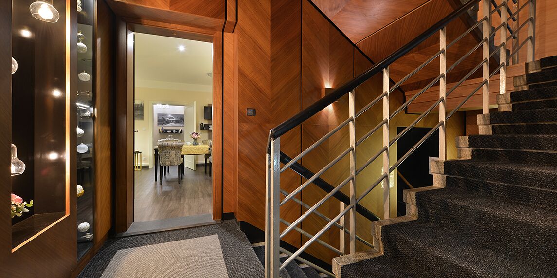 Una escalera con detalles de madera y barandales de metal que conduce a un espacio con zona de comedor al fondo.