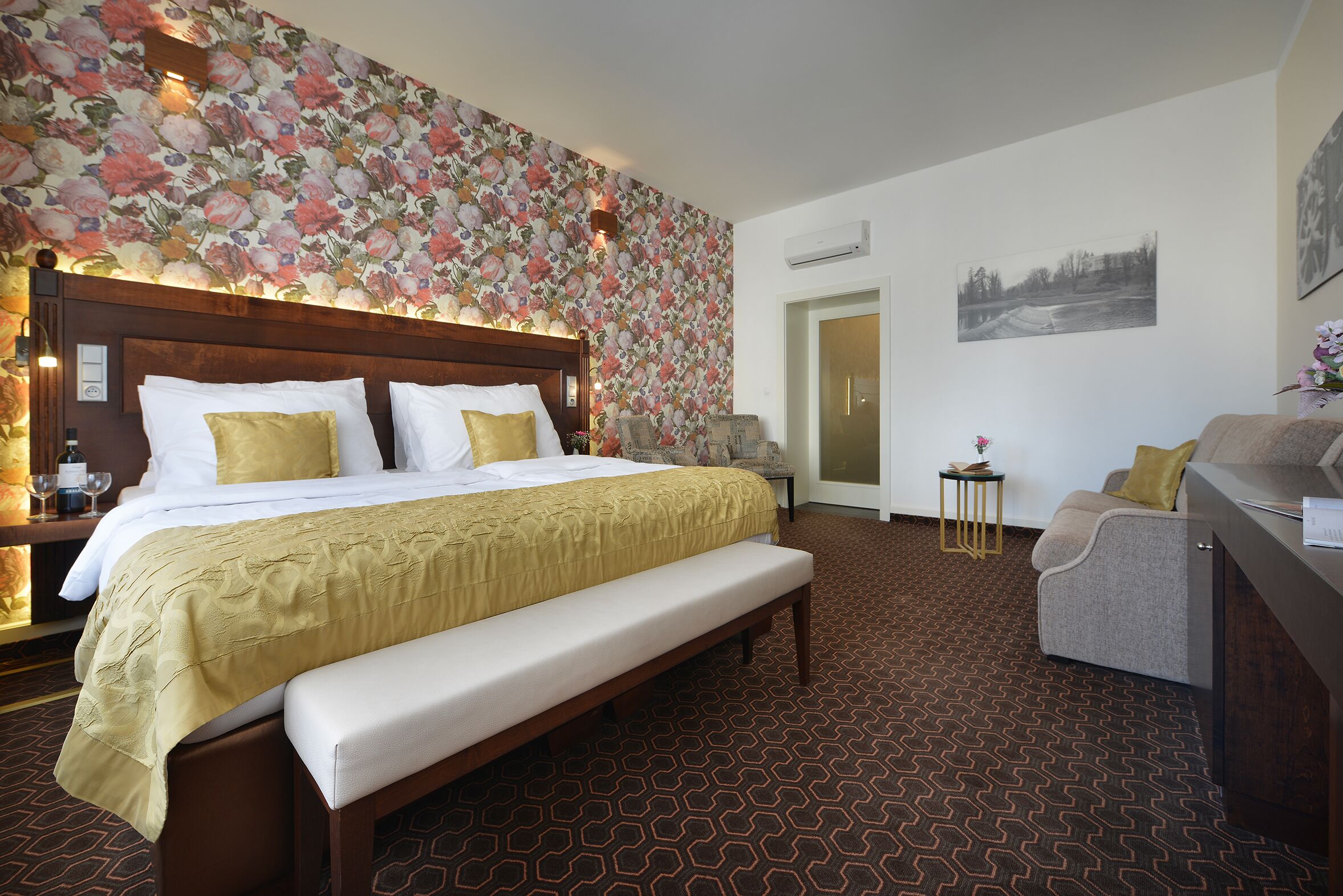 A hotel room with a large bed, a bench, a desk, and a chair.