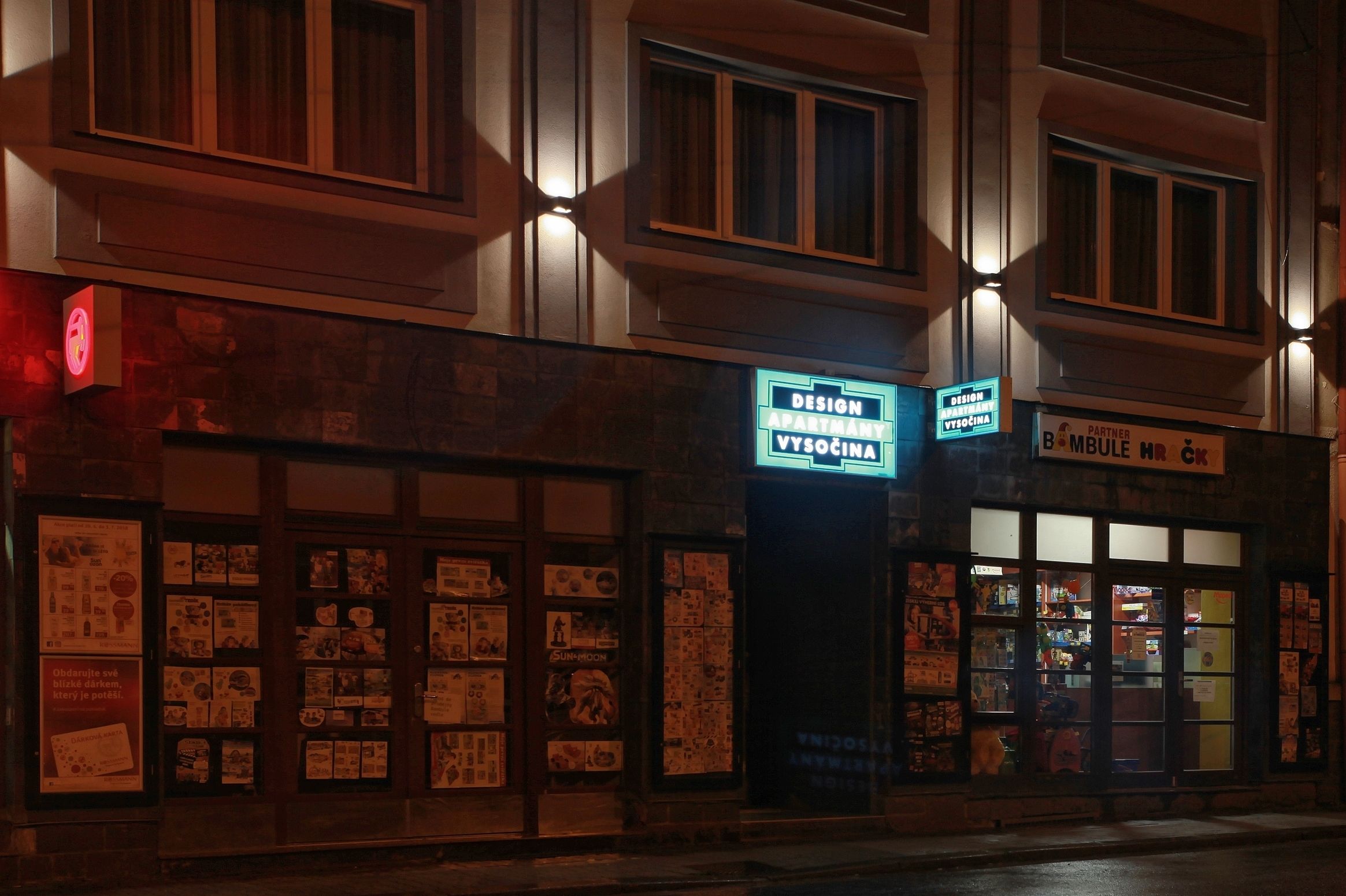 A building with multiple signs, including one for 'DESIGN APARTMENT VYSOCHINA' and another for 'PARTNER BOMBULE'.