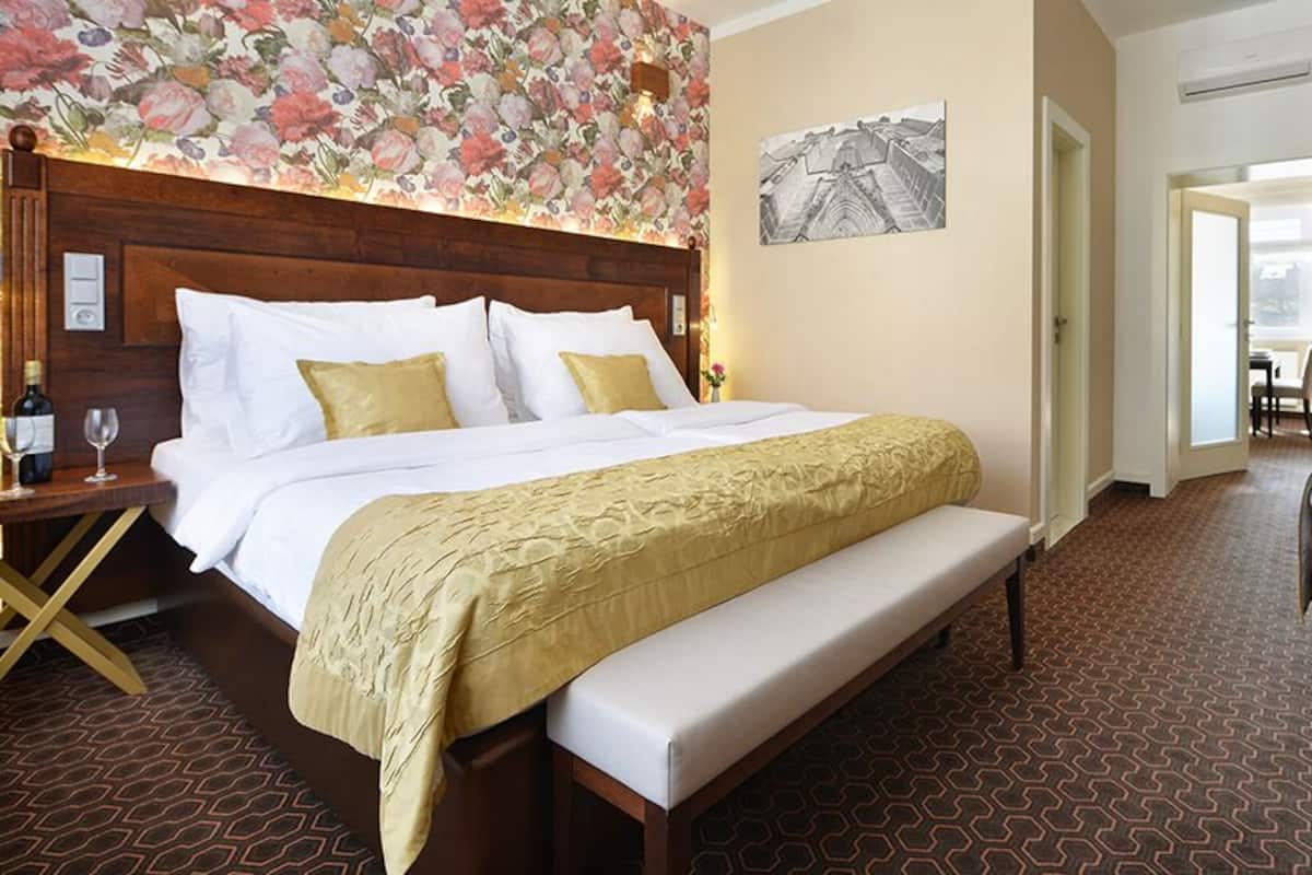 A hotel room with a large bed, a bench, a desk, and a chair.