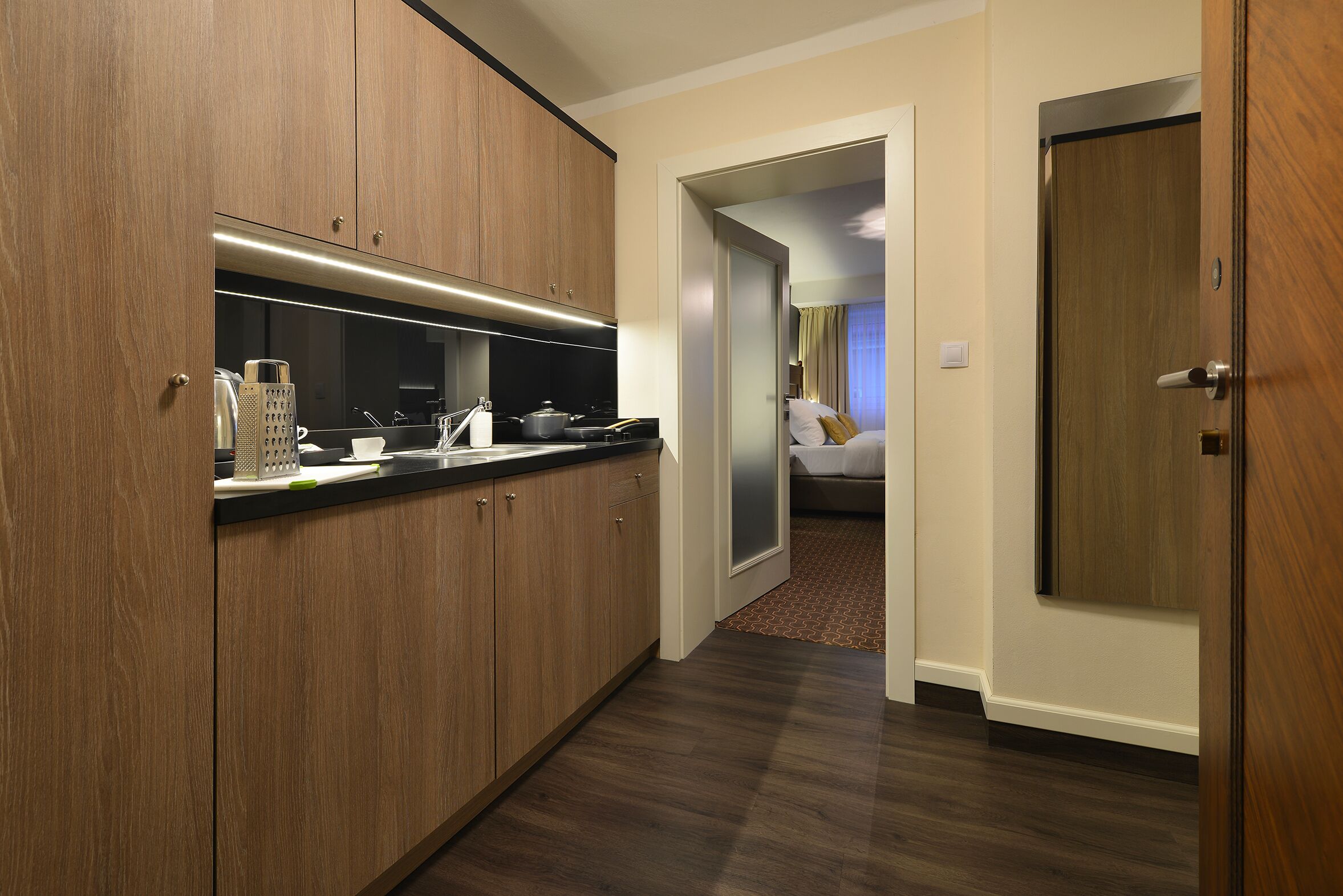 Een moderne hotelkamer met een kitchenette, een bed en een deur die naar een andere kamer leidt.