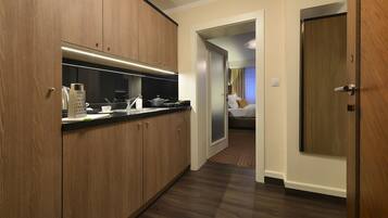 Een moderne hotelkamer met een kitchenette, een bed en een deur die naar een andere kamer leidt.