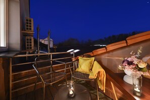 Una terraza con sillas de metal, una mesa pequeña con una vela y un jarrón decorativo con flores.