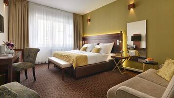 A hotel room with a bed, a desk, a chair, a sofa, and a TV.
