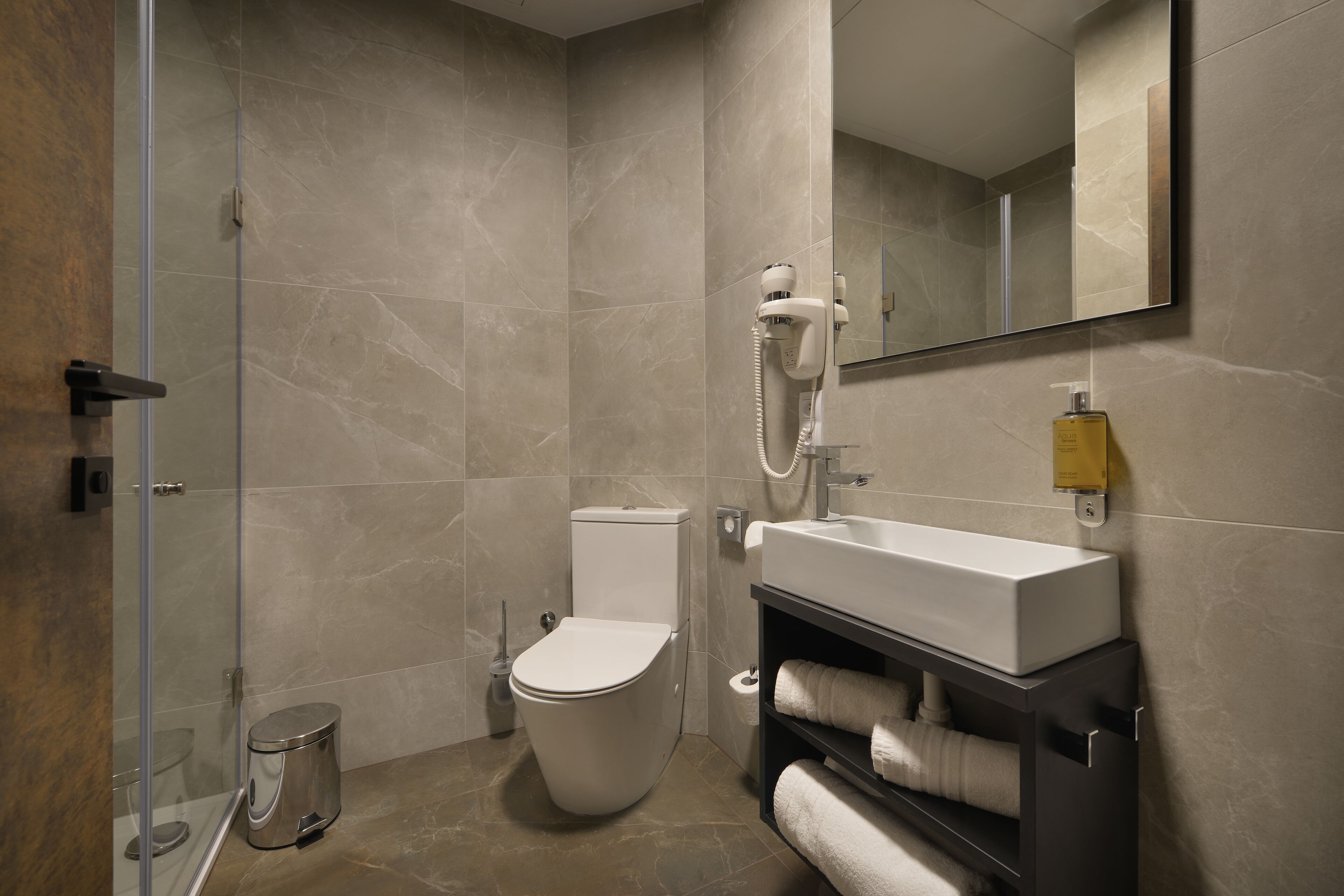 A modern bathroom with a toilet, a sink, a mirror, and a hairdryer.