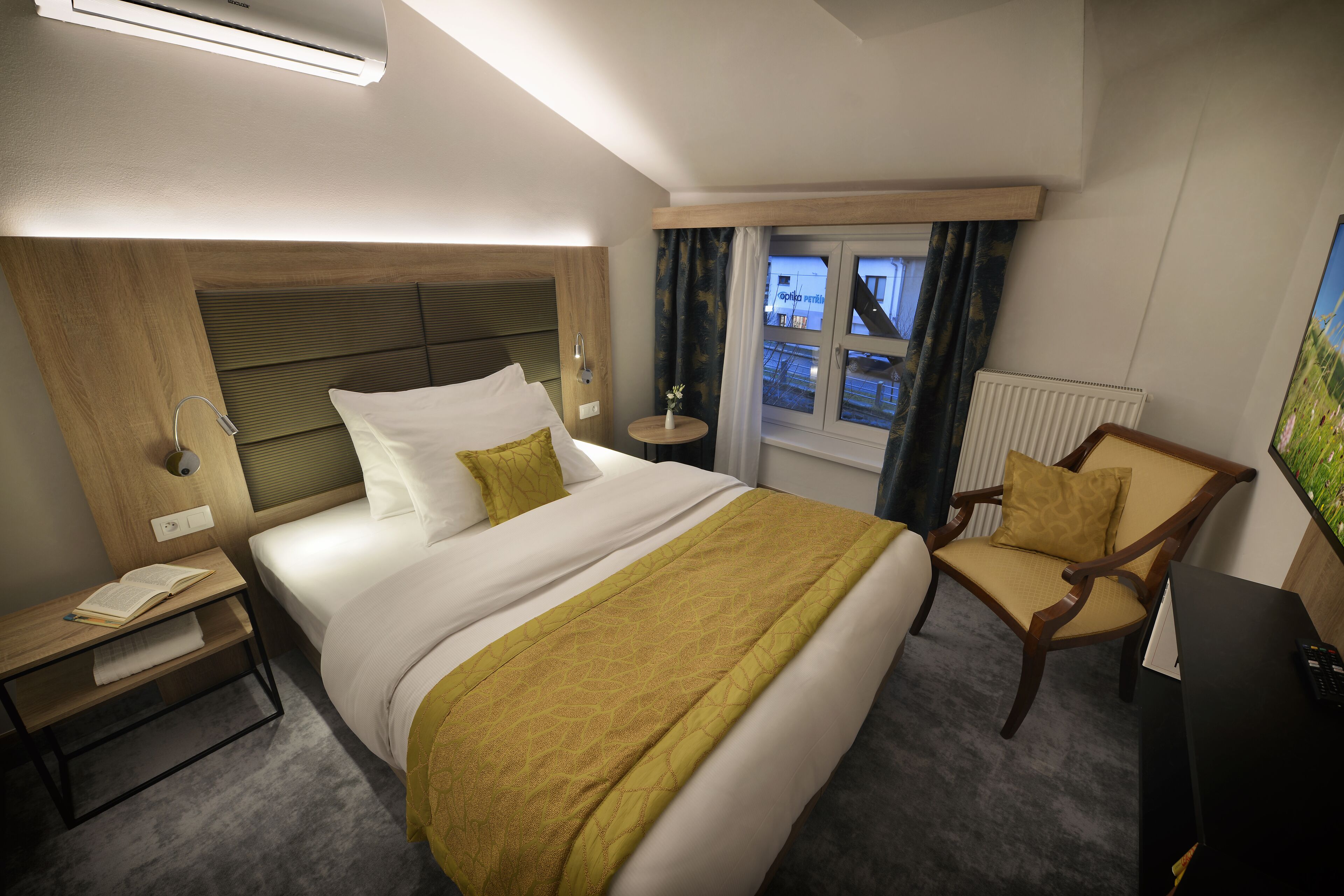 A hotel room with a bed, bedside table, chair, and a view of the outside.