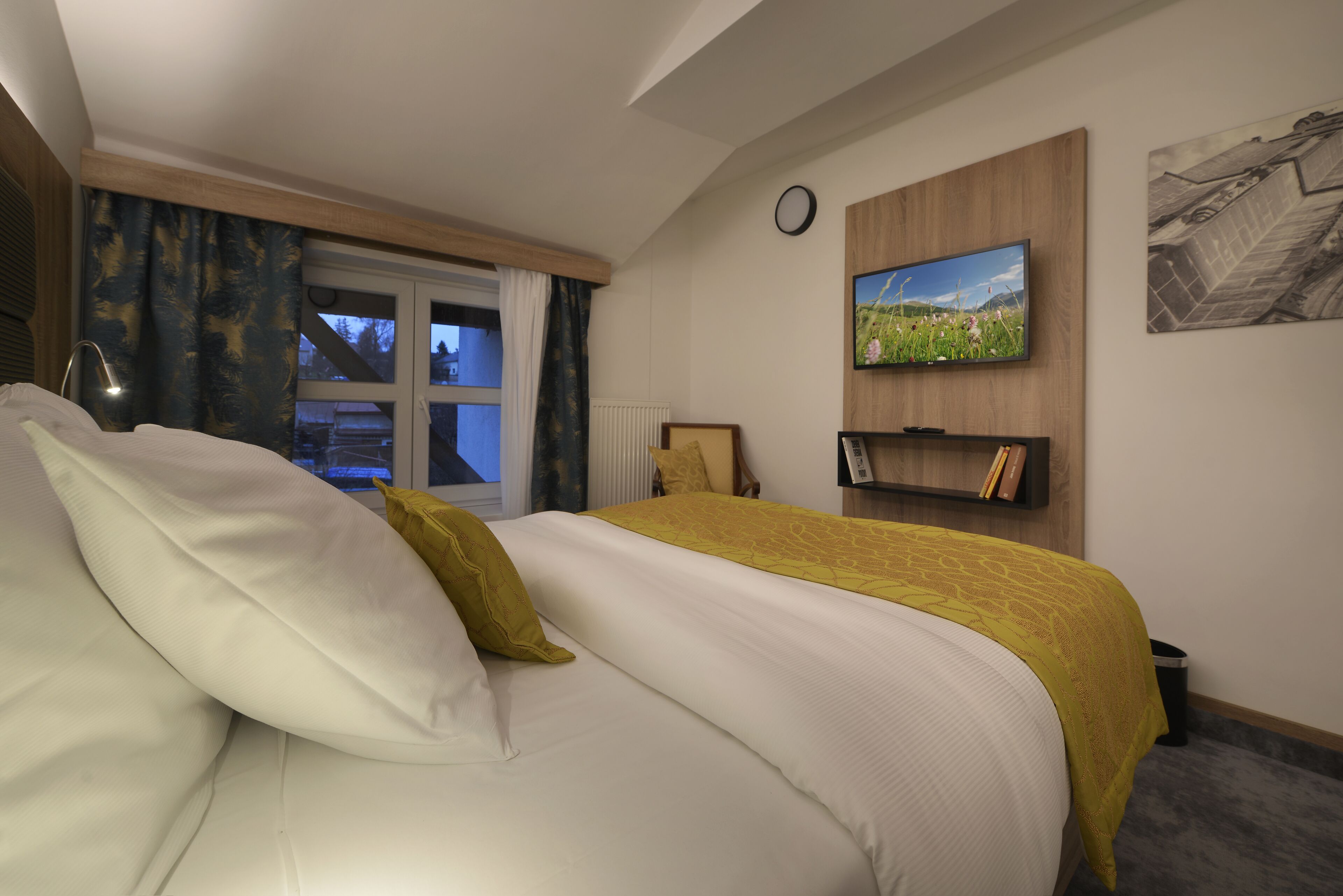 A hotel room with a bed, a TV on the wall, a window with curtains, and a radiator.