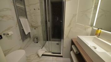 A bathroom with a glass-enclosed shower, a white toilet, and a sink with a mirror.