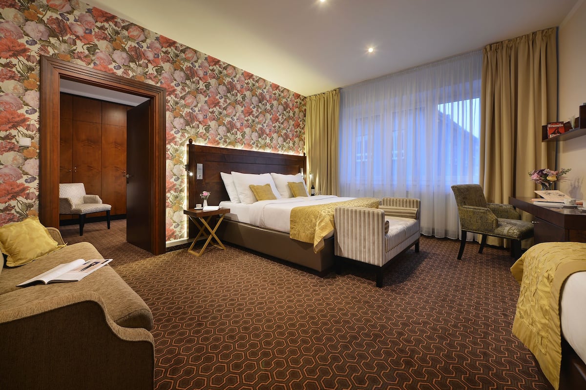 A hotel room with a large bed, a sitting area with a chair, a desk, and a wardrobe.