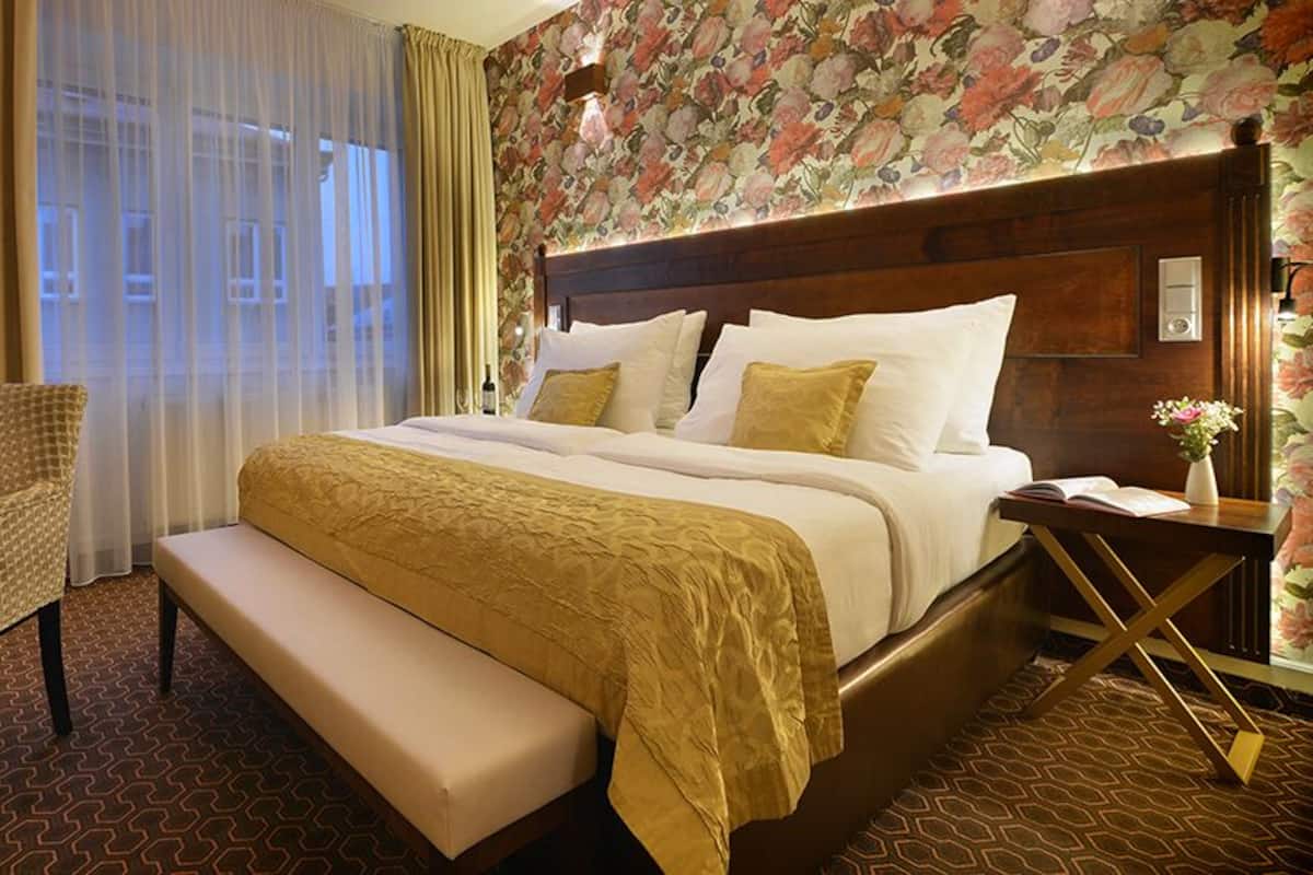 A hotel room with a large bed, a chair, a bench, a desk, and a nightstand.