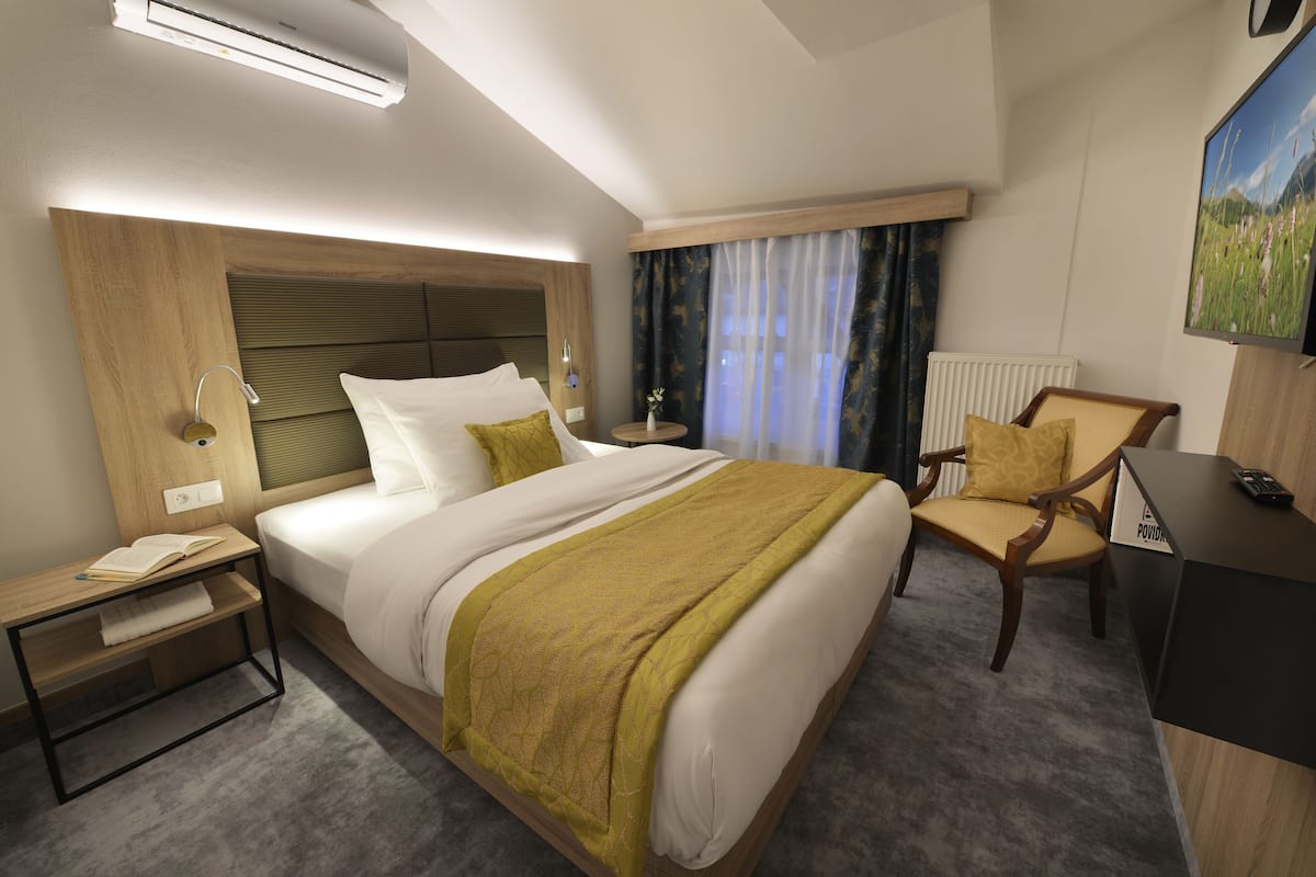 A hotel room with a bed, bedside table, chair, and a desk with a computer.