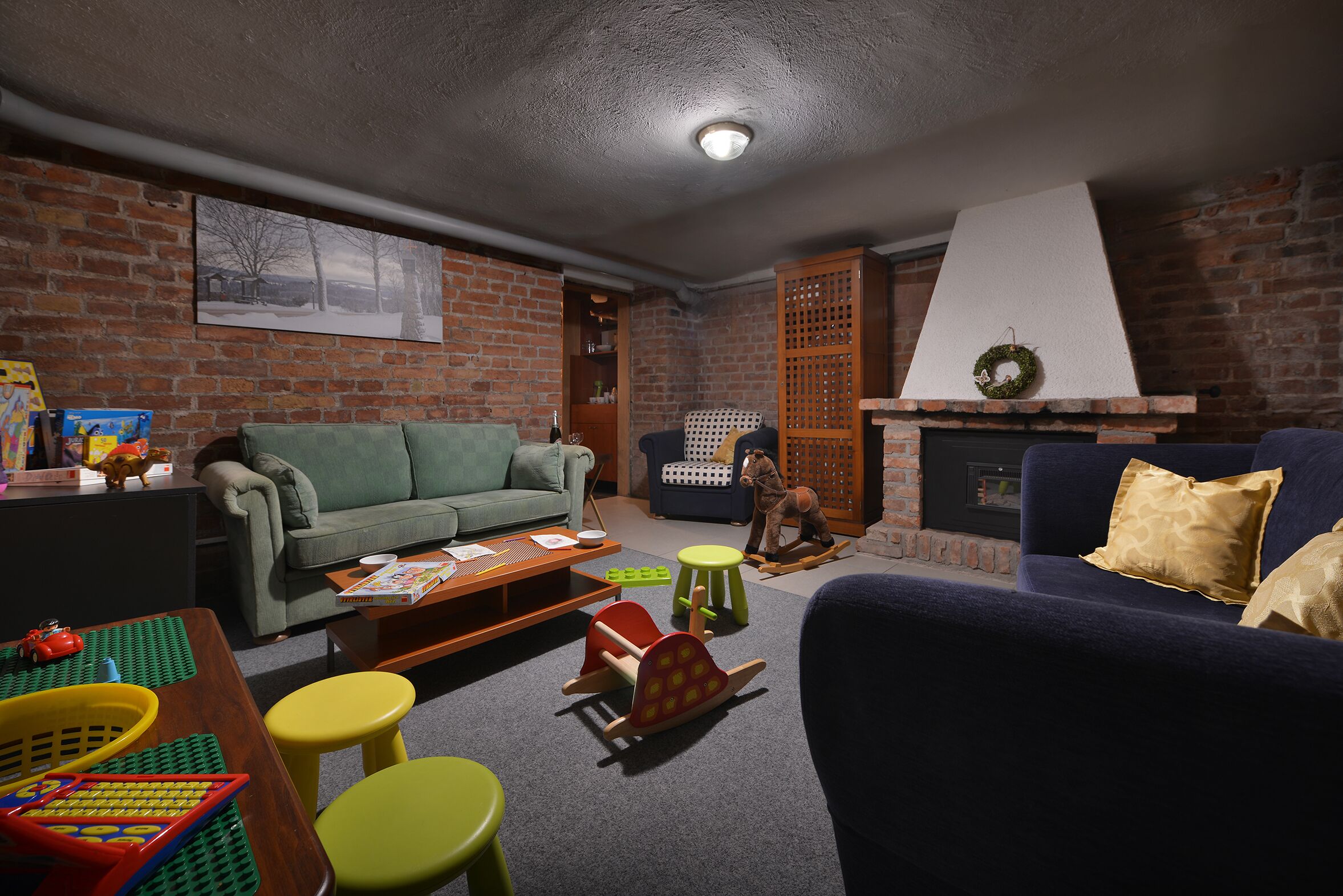 A cozy living room with a brick wall, a fireplace, a green sofa, a blue sofa, and a wooden rocking horse.