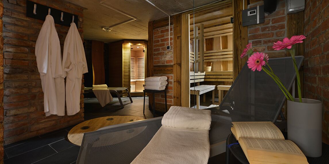 A spa room with a massage table, towels, a wooden chair, and a glass partition.
